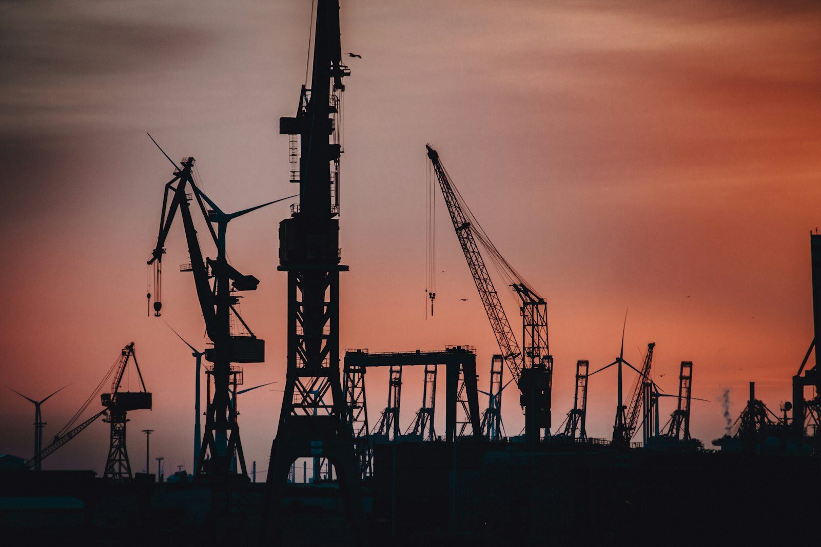 Harbour cranes silhouetted at sunset during vessel operations